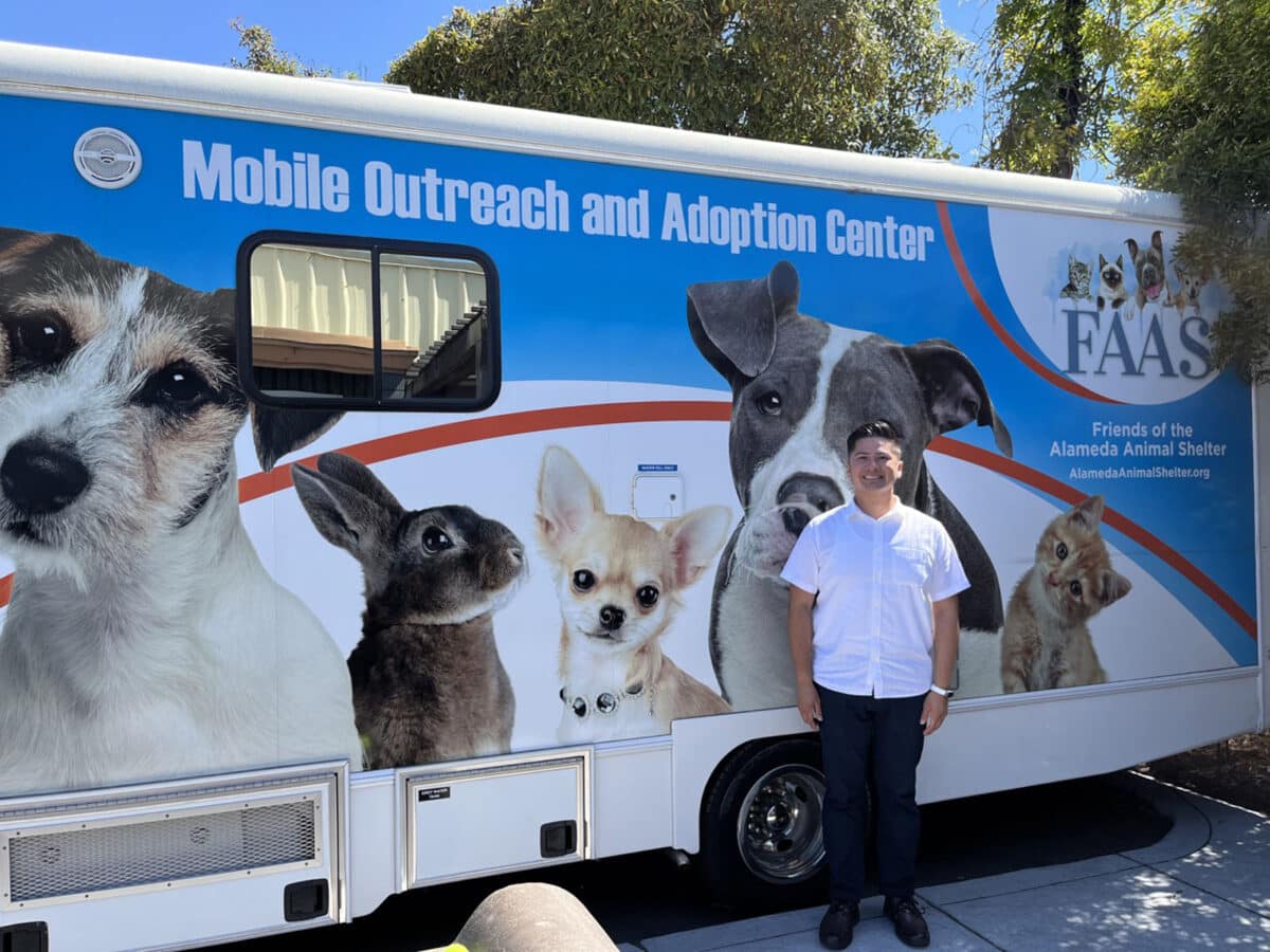 Alameda Post - Adrien Abuyen stands in front of the sign at Friends of the Alameda Animal Shelter's mobile van