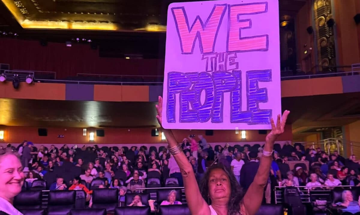 Alameda Post - A woman holds up a "We the People" sign inside the Alameda Theatre.