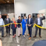 Alameda Post - a group of elected officials and Anthro Energy representatives smile and cut a ribbon in a warehouse