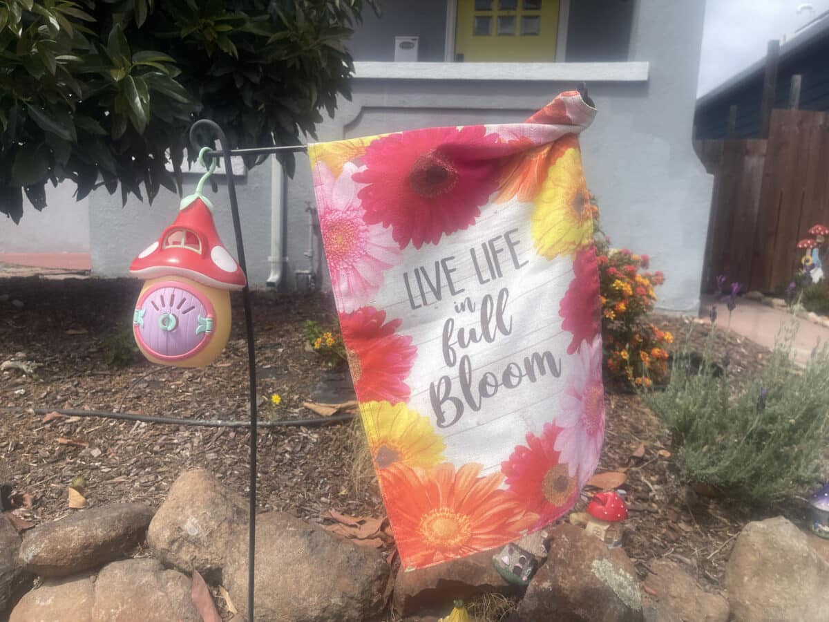 Alameda Post - a sign in a yard that has flowers on it and says "Live Life in Full Bloom"