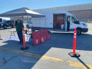 Alameda Post - a worker or volunteer stands next to a row of red waste bins and a large white van at a dropoff station at a StopWaste event