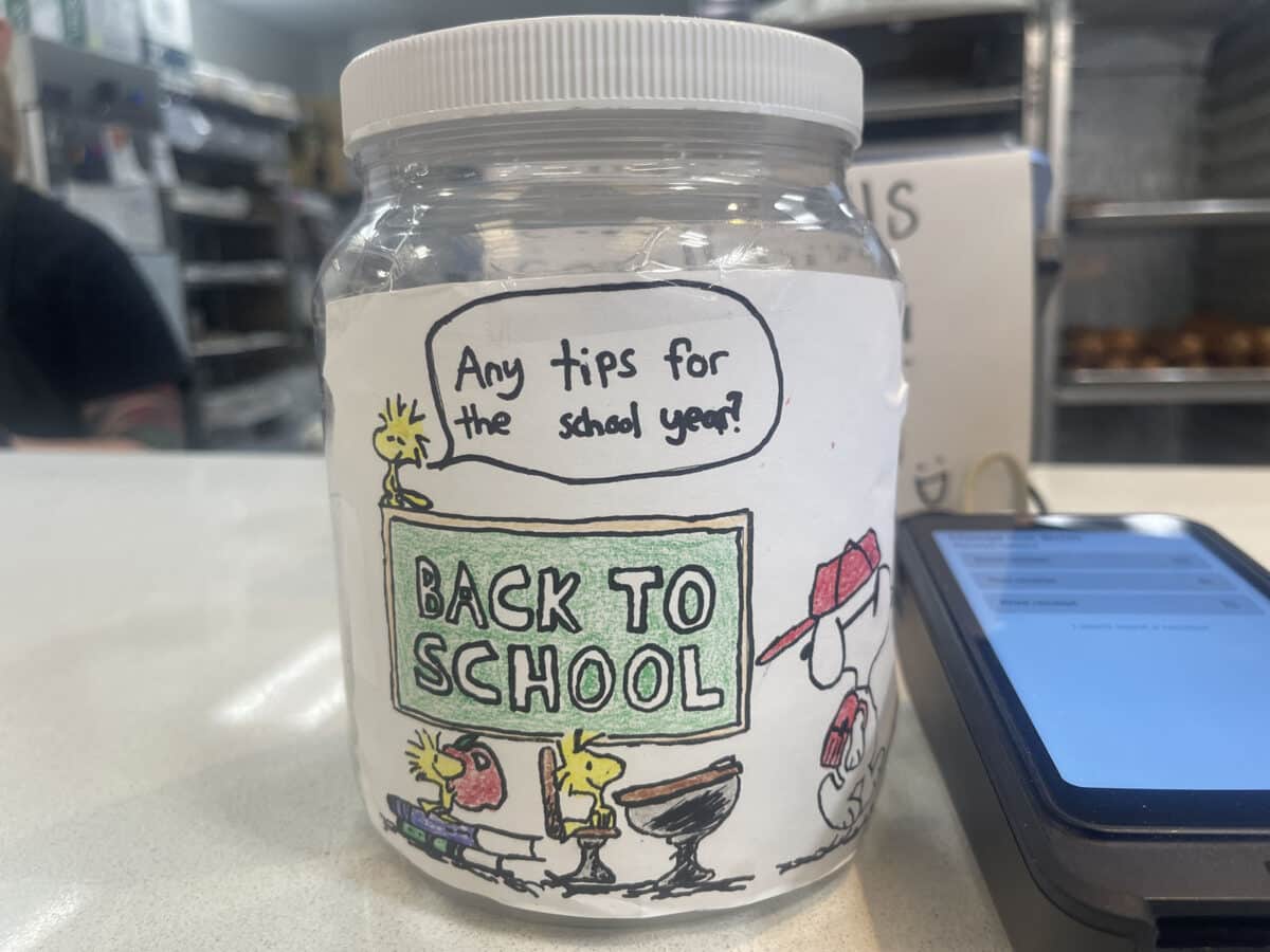 Alameda Post - a tip jar with drawings of Peanuts characters sitting in a school setting. It says, "Any tips for the school year?"