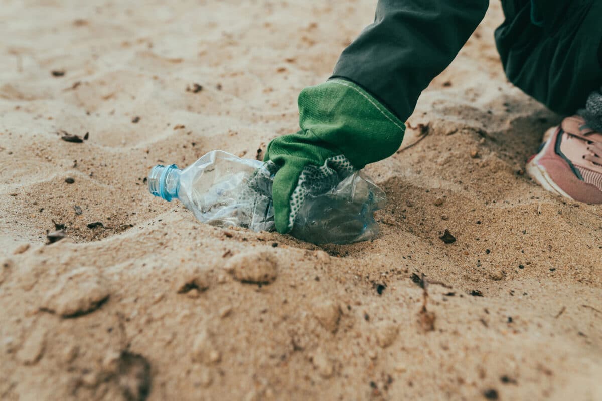 Alameda Post - a person picks up a water bottle from the beach