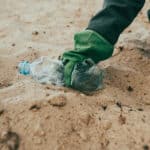 Alameda Post - a person picks up a water bottle from the beach