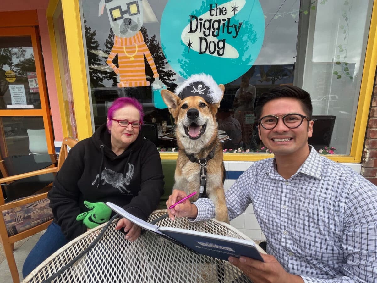 Alameda Post - Mouf the dog sits at an outdoor table with two smiling people in front of The Diggity Dog.