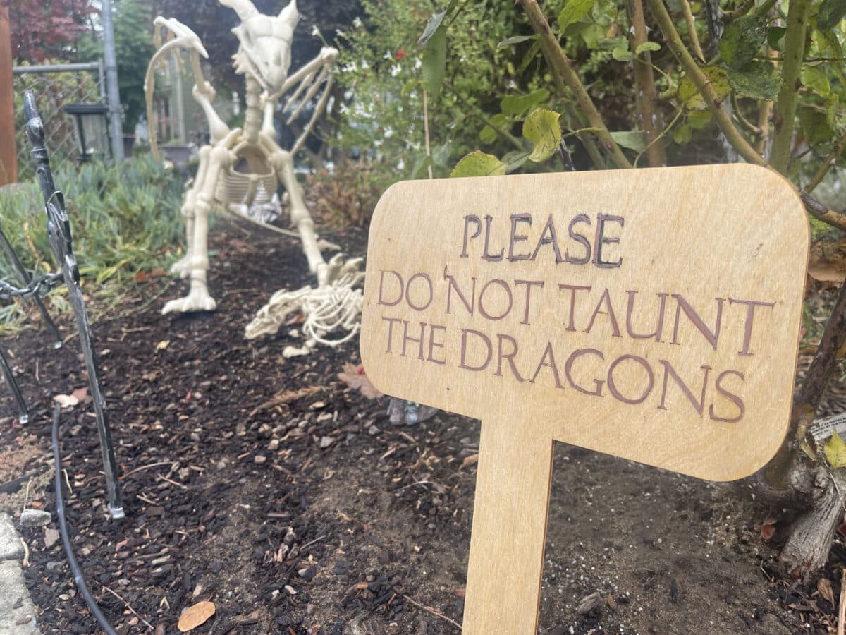 Alameda Post - A sign in a lawn that says "Please do not taunt the dragons" next to decor of dragon skeletons.