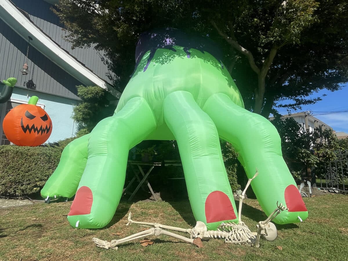 Alameda Post - A huge inflatable witch hand on a yard. It looks like it's materialized from a portal in a tree.