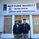 Alameda Post - The new owners of Neptune Market stand in front of the store's doors and smile.