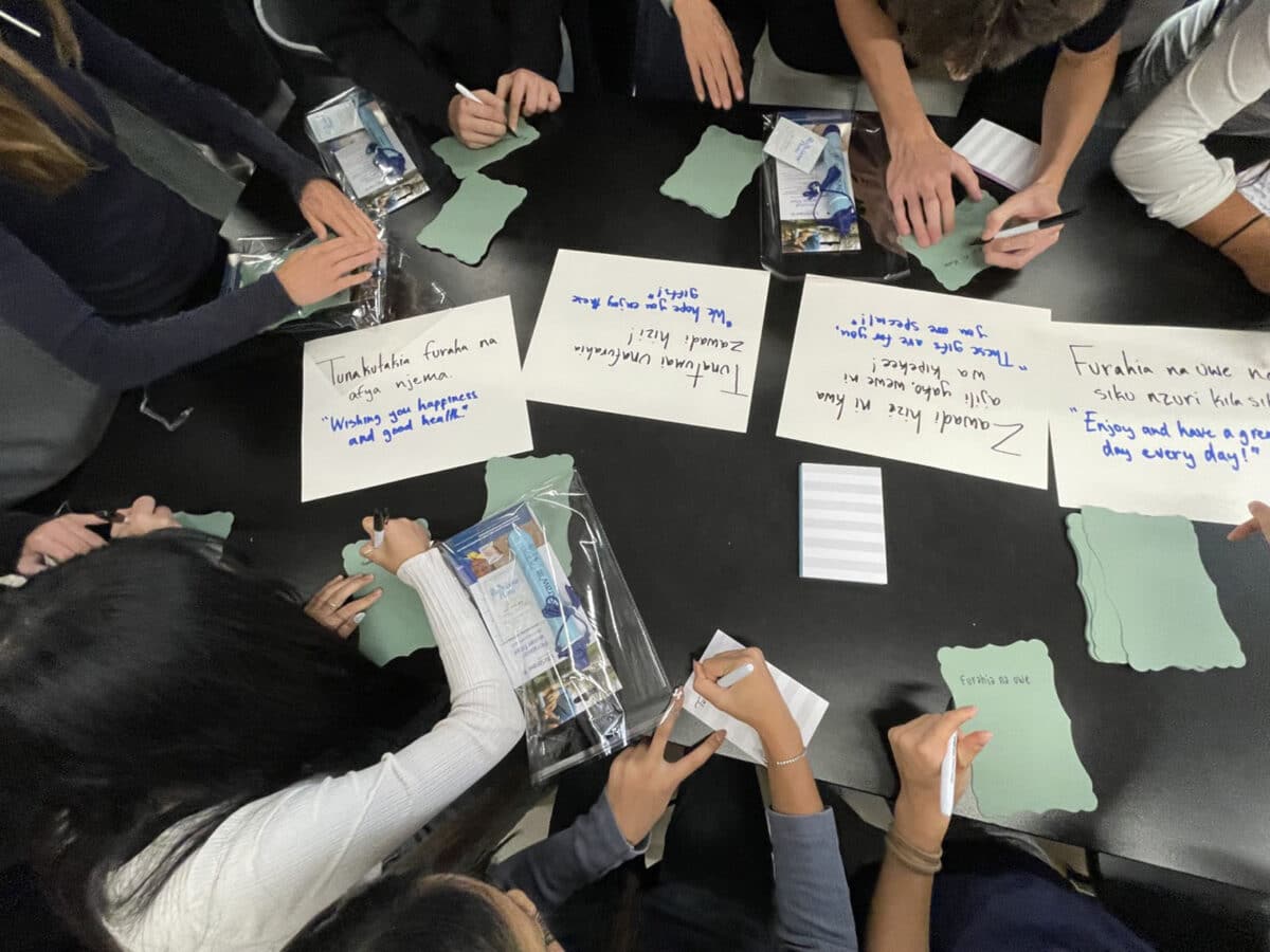 Alameda Post - Students write notes to go in the AguaEmpowers bags. On the table in front of them are written out sayings for them to copy, along with the English translations.