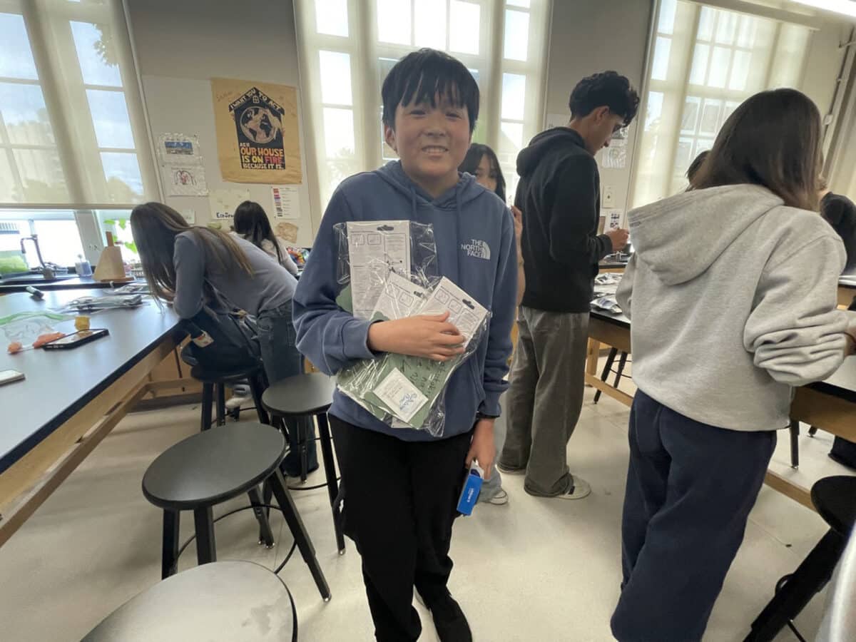 Alameda Post - A high school student stands amongst peers assembling kits and smiles. 