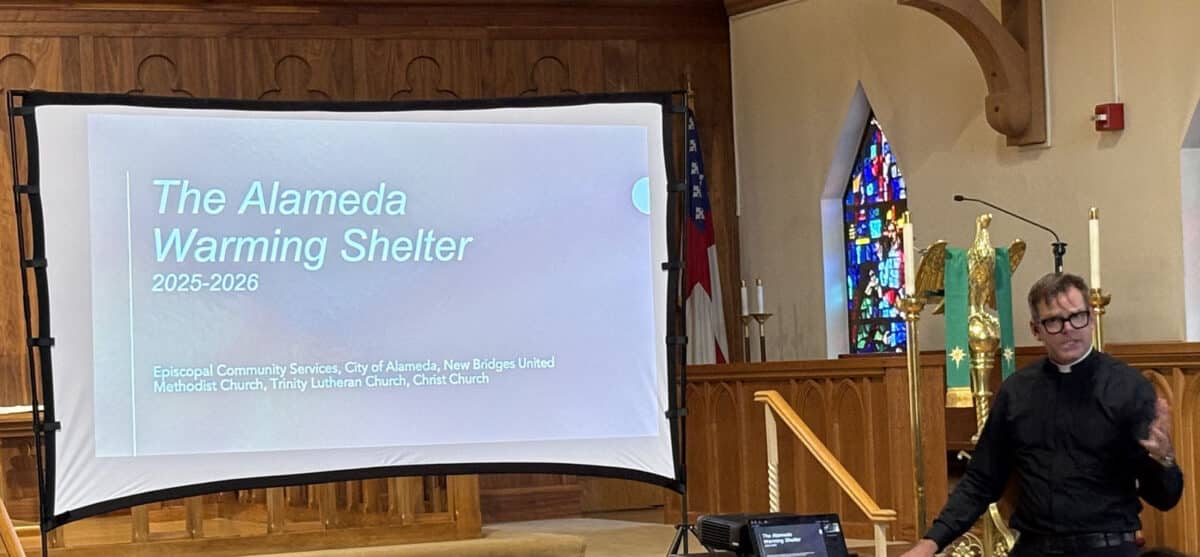 Alameda Post - Rev. Stephen McHale stands at the front of Christ Episcopal Church with a projection on a screen that says "The Alameda Warming Shelter."
