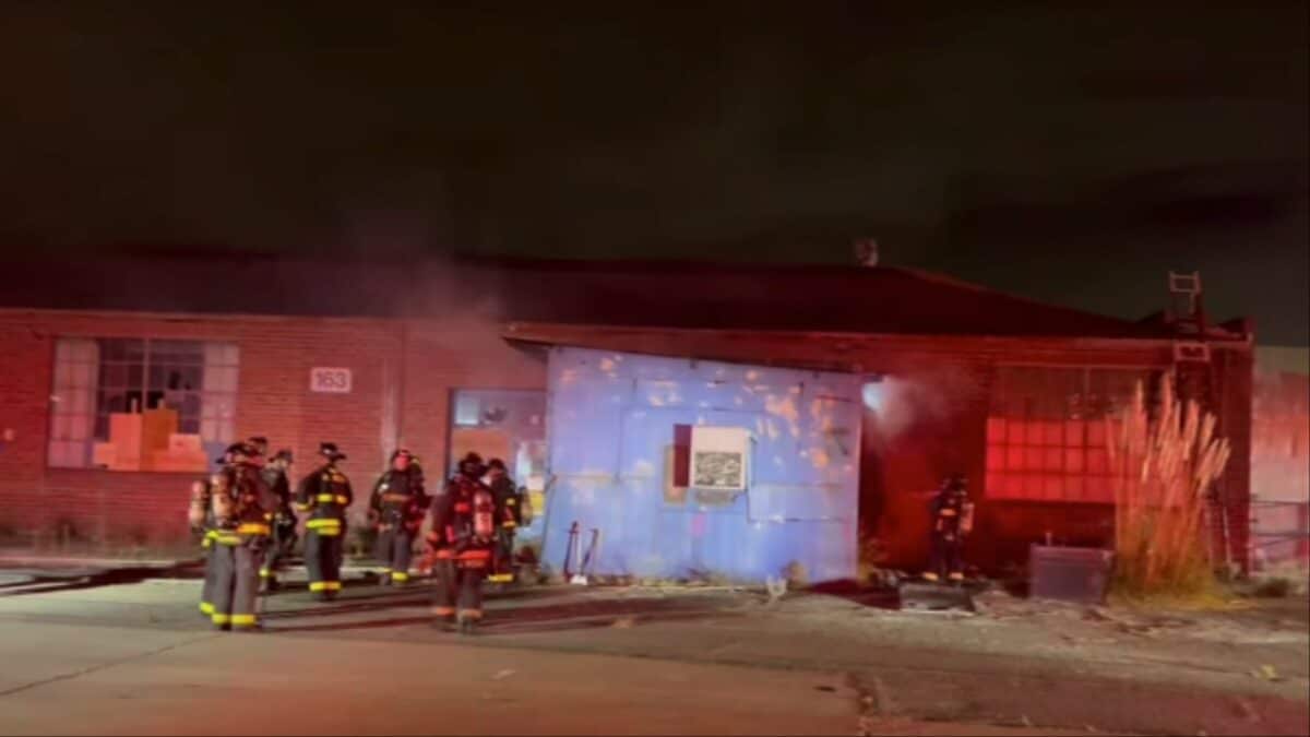 Alameda Post - Firefighters congregate in the dark, in front of a warehouse or commercial building.