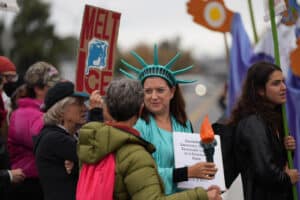 Alameda Post - A gathering of protestors, including a woman in a Statue of Liberty outfit and someone with a "Melt Ice" sign.