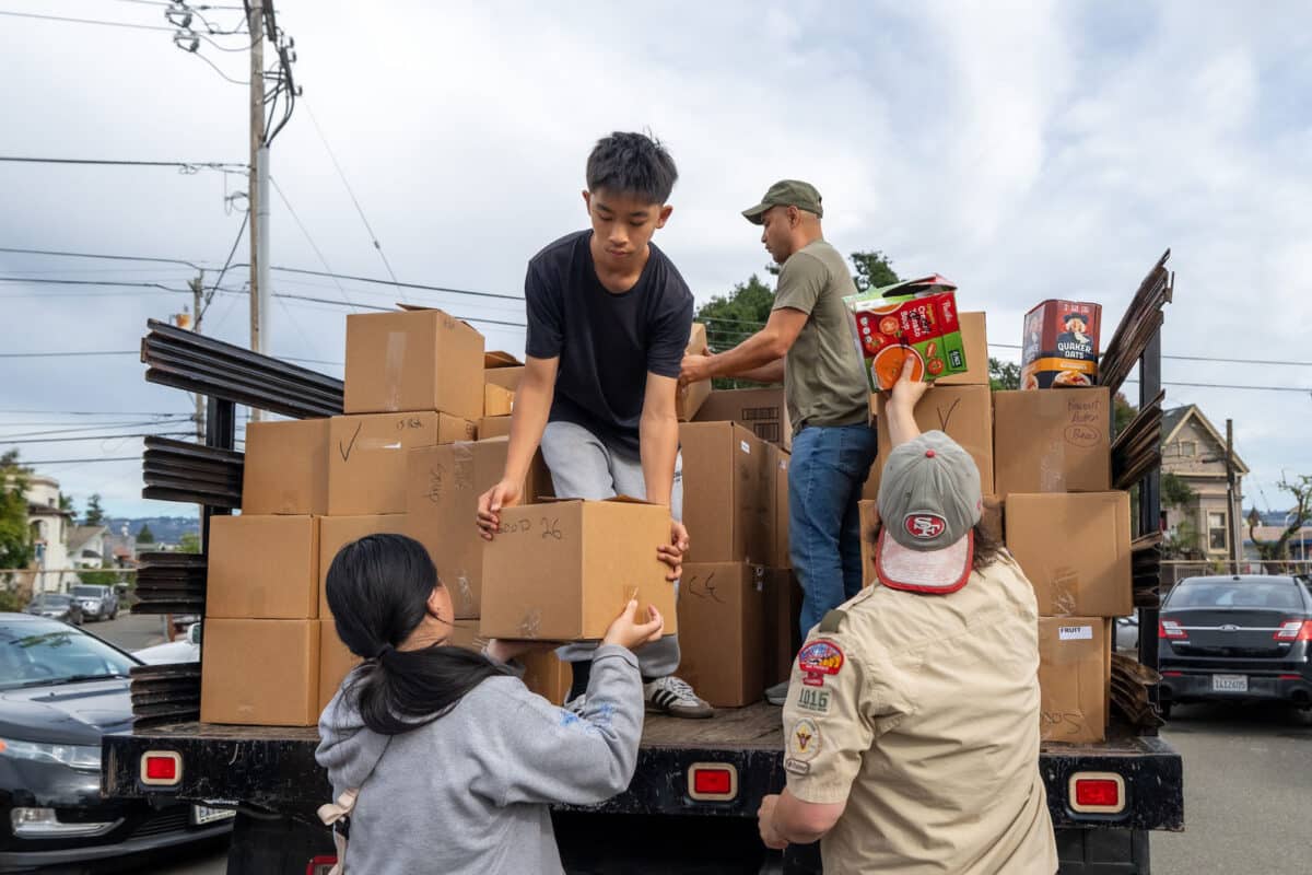 Alameda Post - Scouts and adult volunteers load cardboard boxes of food into a truck. 