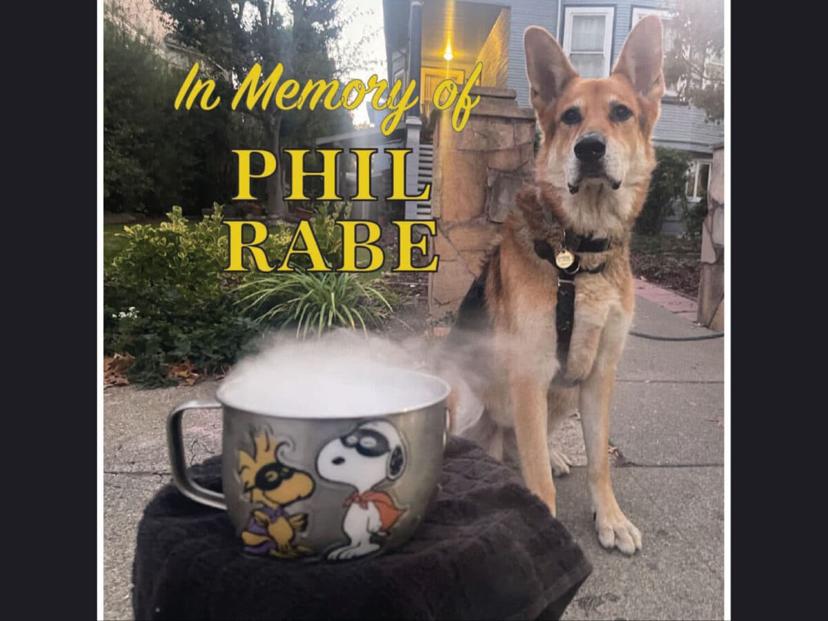 Alameda Post - Mouf the dog sits in front of a Halloween mug that is steaming with dry ice. Text over the top says "In Memory of Phil Rabe."