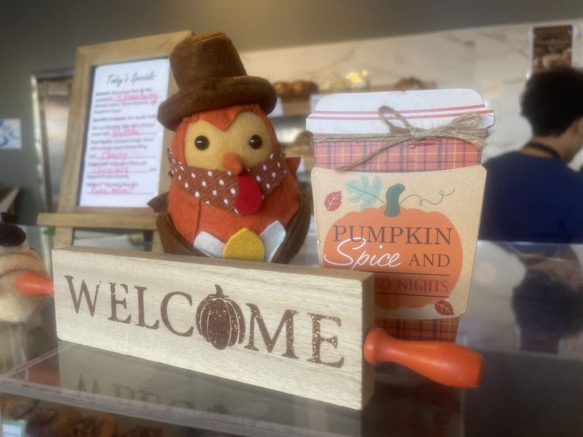 Alameda Post - On the counter of a coffee shop, a decoration of a turkey sits next to a Welcome sign and a Pumpkin Spice Latte decoration. 