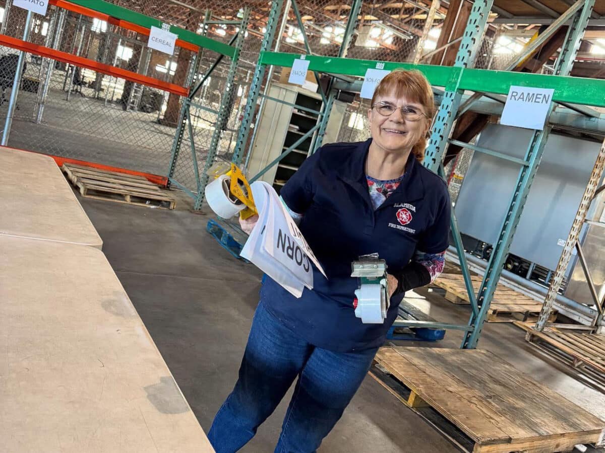 Alameda Post - A woman from the Alameda Fire Department smiles and holds papers and tape. 