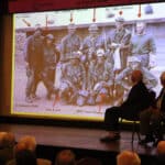 Alameda Post - Onstage at the Alameda Elks Lodge, a slideshow shows an old photo of servicemembers from the Vietnam War.