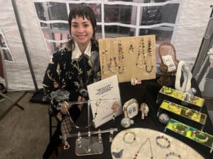 Alameda Post - A vendor at Queer Canvas smiles at their table of jewelry.