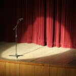 Alameda Post - A microphone onstage with a spotlight in front of a red velvet curtain.