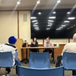 Alameda Post - The Home Match director and another person sit at the front of a room at the library and talk.