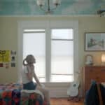 Alameda Post - A girl who appears to be in her teens sits on the bed of a childhood bedroom and talks on the phone.