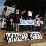 Alameda Post - A line of beach protestors hold signs that say things like "Hands Off!" " Venezuela's Oil!" and "Free Epstein."