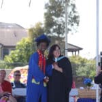Alameda Post - A teacher stands onstage and hands a diploma to a student. They both smile.