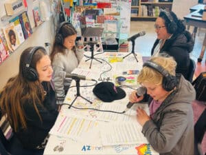 Alameda Post - Four elementary schoolers and one adult sit around a table with podcast equipment. They are recording the February Little Minds Big Talks podcast.