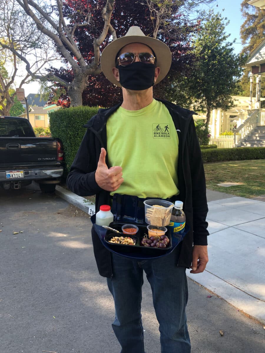 Alameda Post - A person out for a walk wearing a mask and a fanny pack with a whole tray of snacks. 