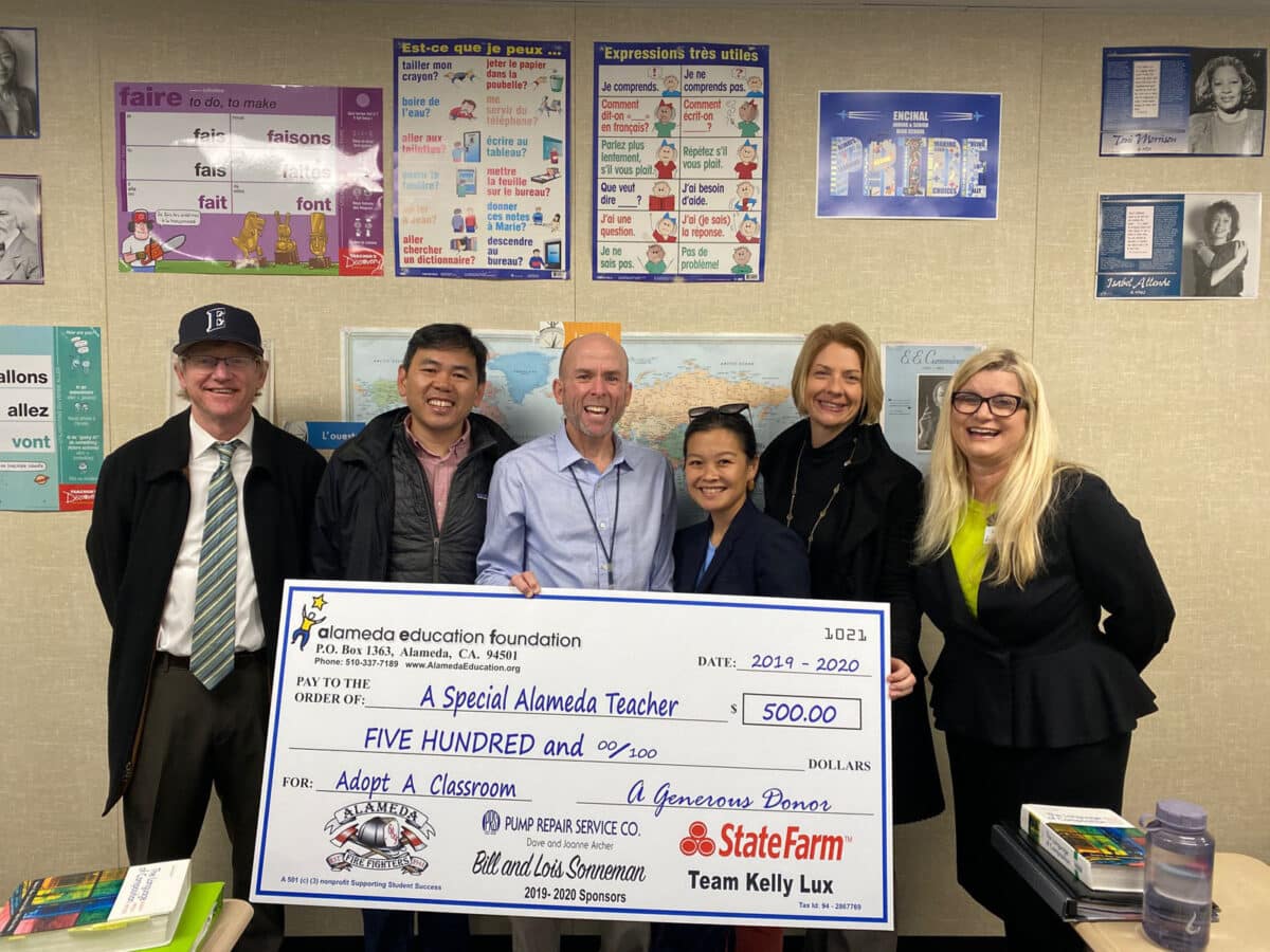 Alameda Post - Kevin McNulty smiles and holds a large check from AEF next to five other people. 