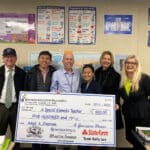 Alameda Post - Kevin McNulty smiles and holds a large check from AEF next to five other people.