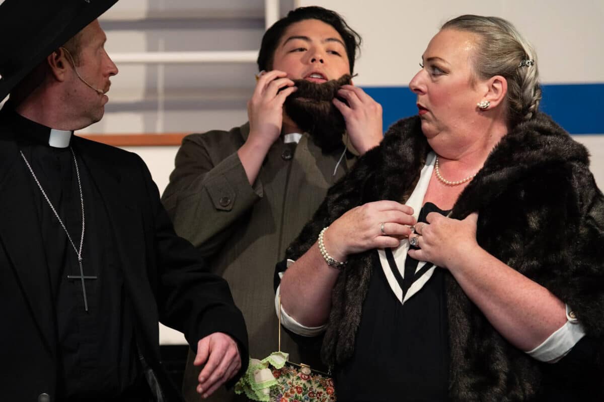 Alameda Post - A priest, a woman in a fur coat, and a man holding a fake beard together onstage.