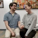 Alameda Post - Two actors sit on a bench or seat and look at each other affectionately. They are in the lobby of the Food Bank performing Much Ado About Nothing.