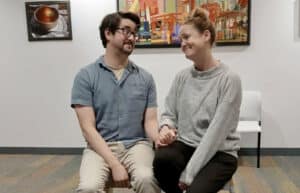 Alameda Post - Two actors sit on a bench or seat and look at each other affectionately. They are in the lobby of the Food Bank performing Much Ado About Nothing.