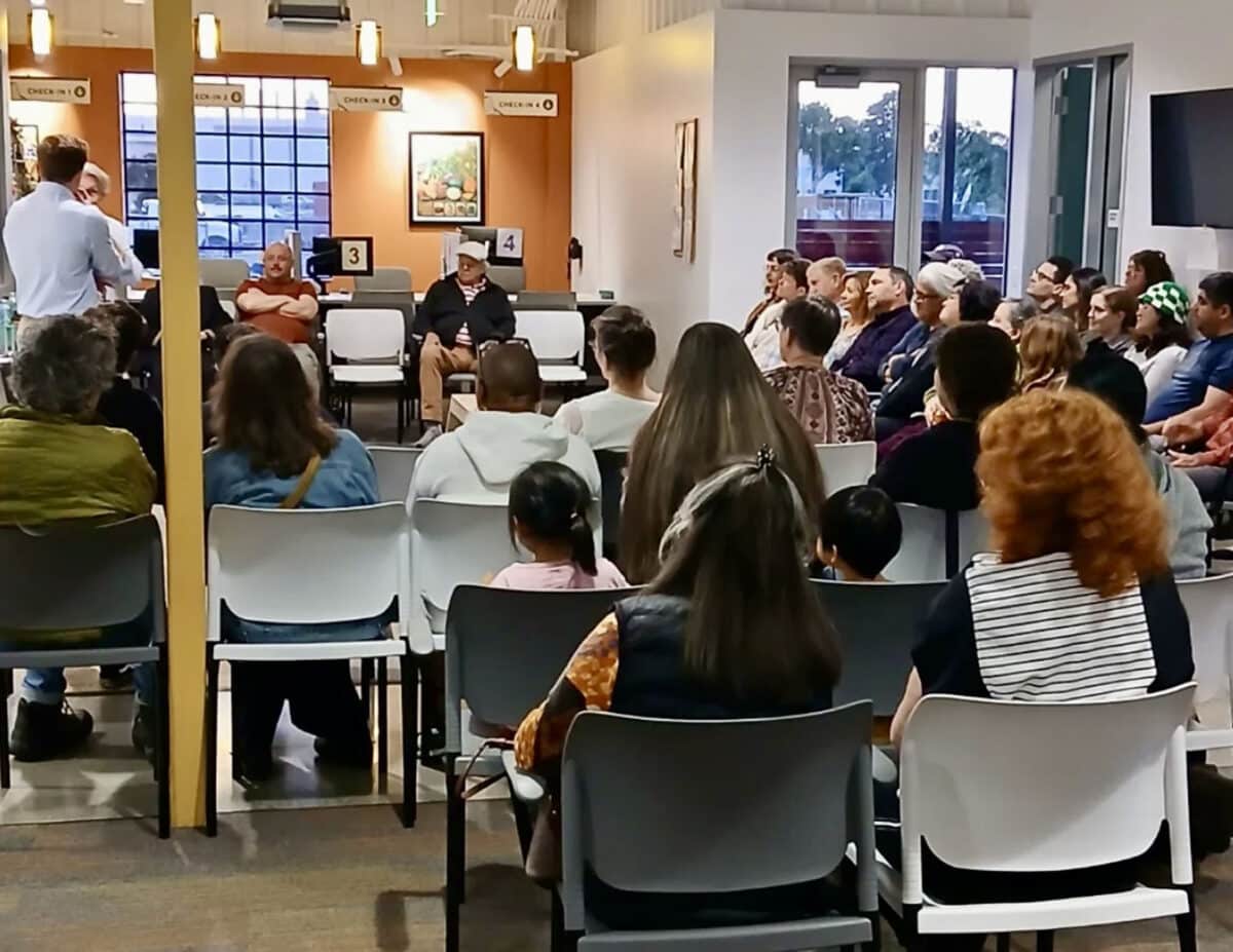 Alameda Post - The lobby of the Food Bank with a crowd seated in chairs watching a play. 
