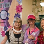 Alameda Post - Three women dressed as grannies smile next to an Alameda GrannyCon sign.