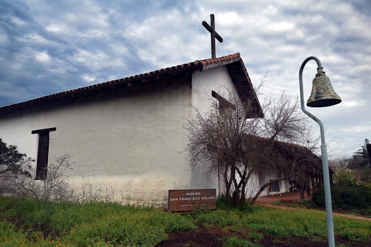 Alameda Post - A classic mission building with a cross on top and a bell outside.