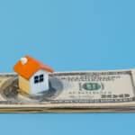 Alameda Post - A small model of a house on top of a stack of money.