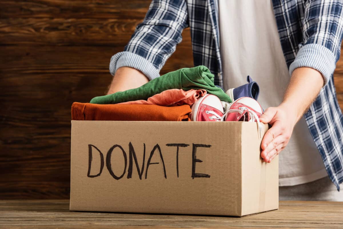 Alameda Post - A person grabs a cardboard box of clothes and shoes labeled "donate."