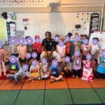 Alameda Post - A smiling adult sits with a class full of elementary schoolers with flower emojis over their faces.