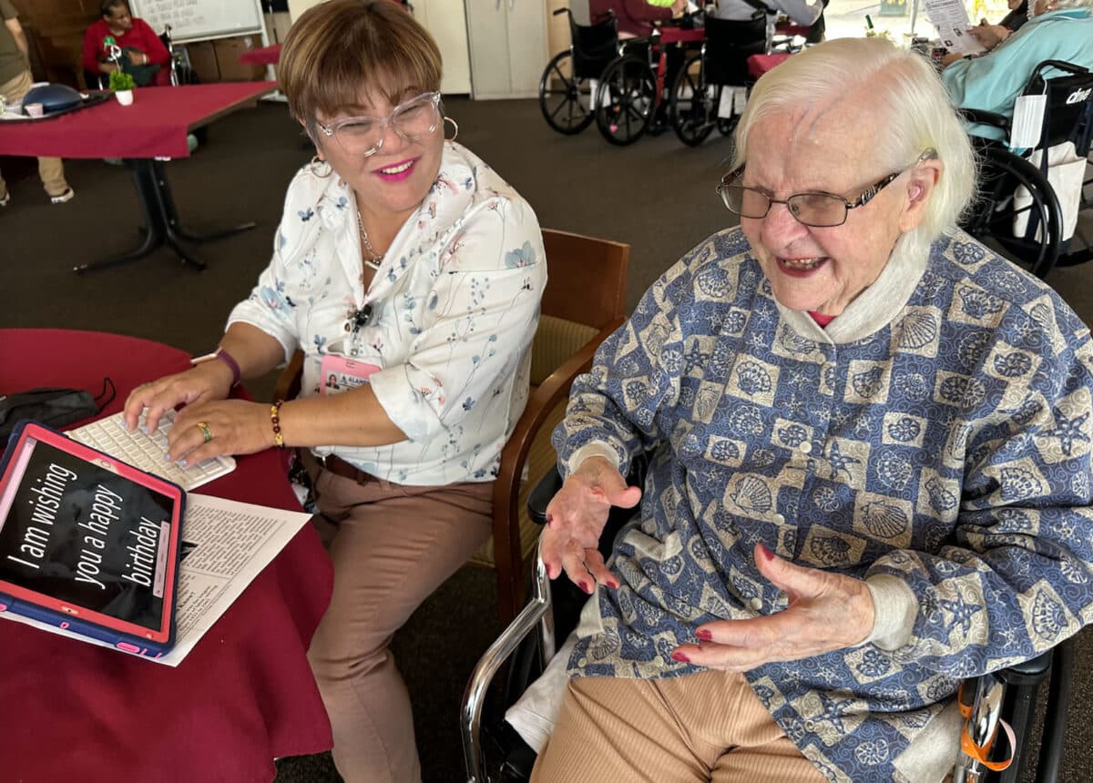 Alameda Post - An Alameda Health System sits next to a smiling older women. 