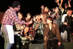 Alameda Post - A youg man sings to a young woman onstage with an enthusiastic ensemble behind them.