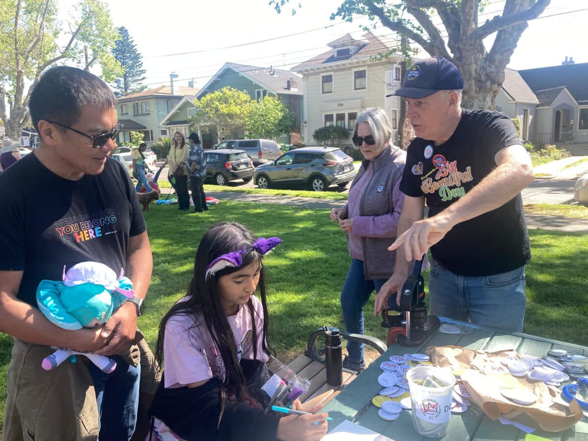 Alameda Post - A young girl sits at a table completing a craft, while a volunteer talks with an adult by her side. 