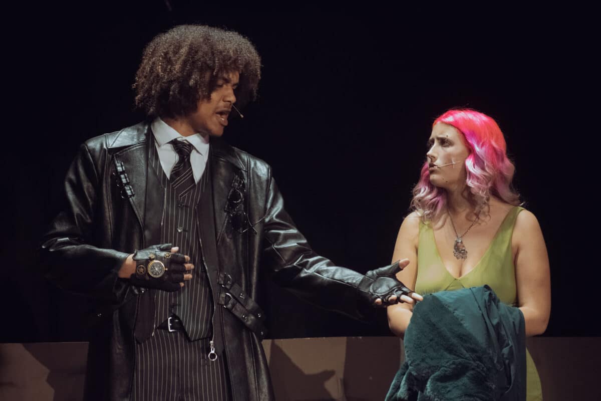 Alameda Post - A young actor in a sharp black pinstriped suit and leather, and a young actress with bright pink hair and a light green dress. 