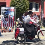 Alameda Post - A woman rides a tricycle in the Fourth of July parade. She had a No Kings sign on the back.