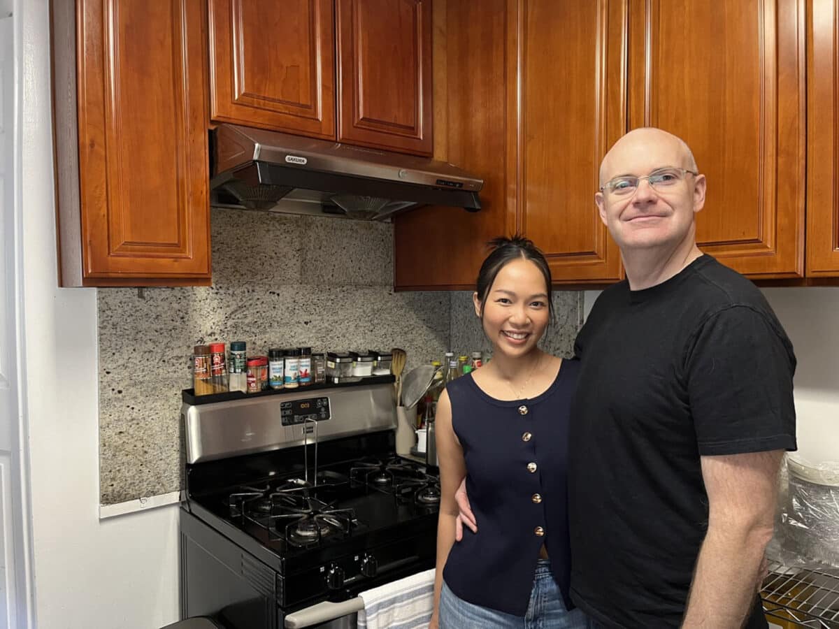 Alameda Post - A man and woman stand together in a home kitchen and smile. 