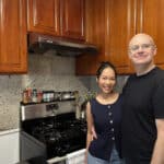 Alameda Post - A man and woman stand together in a home kitchen and smile.