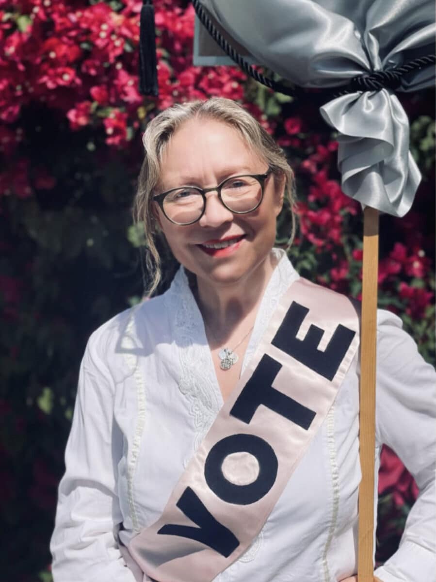 Alameda Post - A vote smiles, wearing a Vote banner.