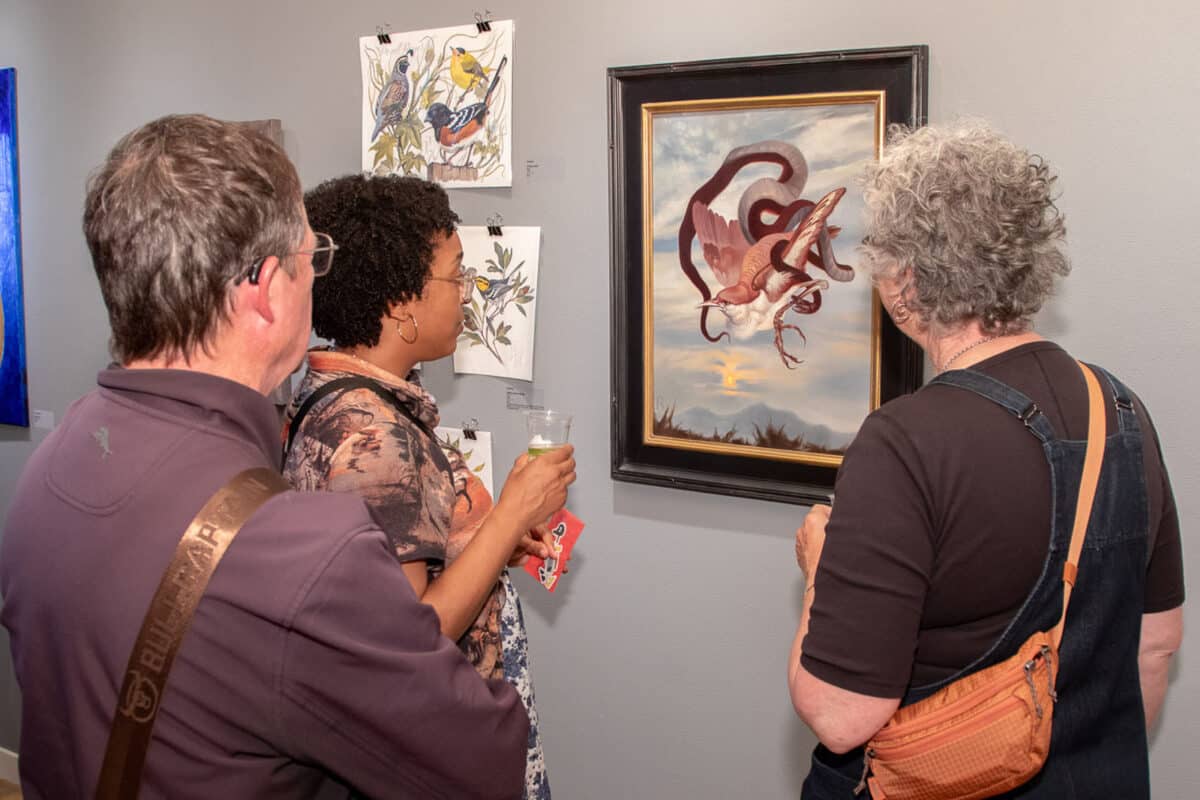 Alameda Post - Visitors to Rhythmix Cultural Works gather around an artwork of an entangled bird and serpent.